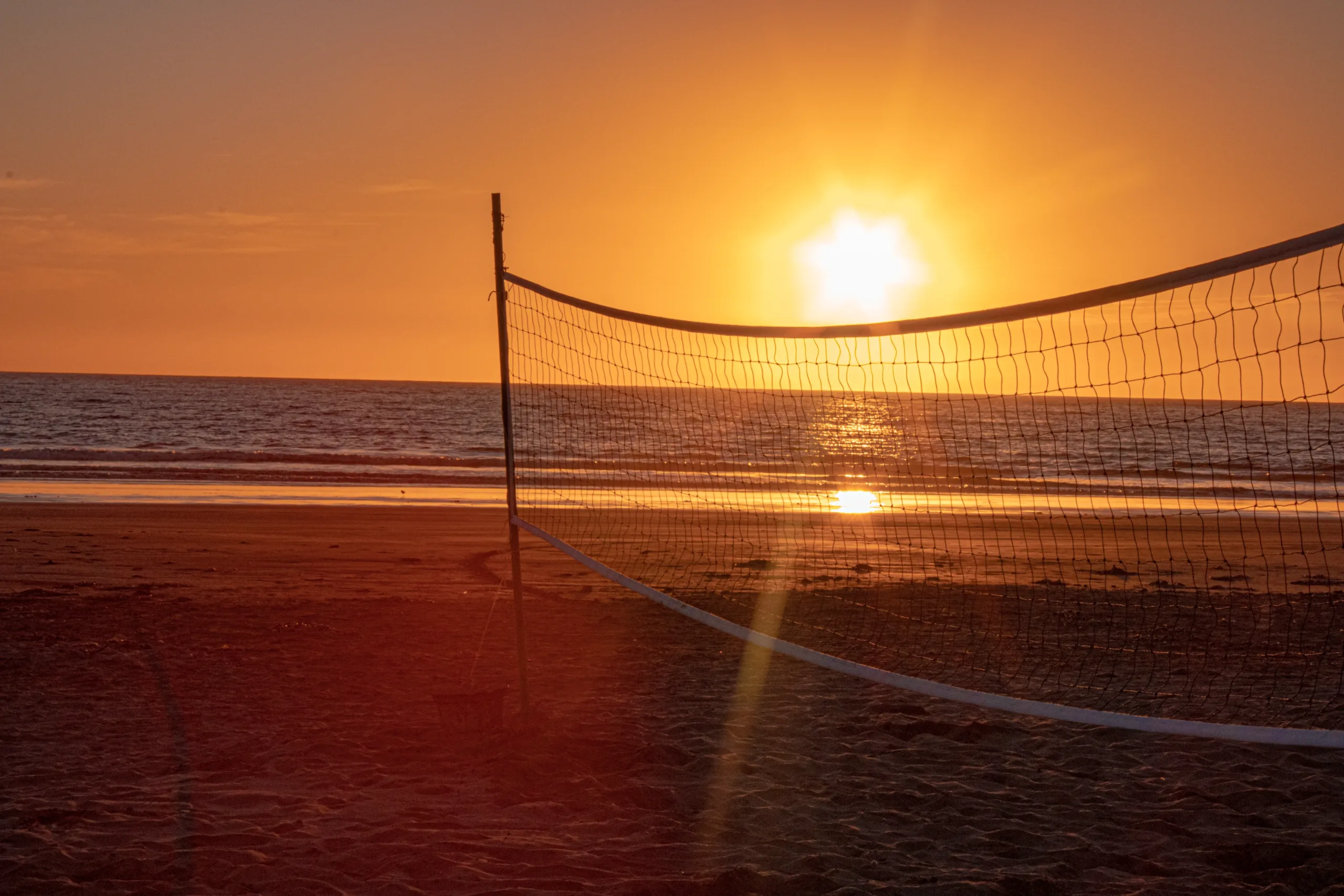 Red de voleibol en la playa con vista al mar durante un atardecer dorado.